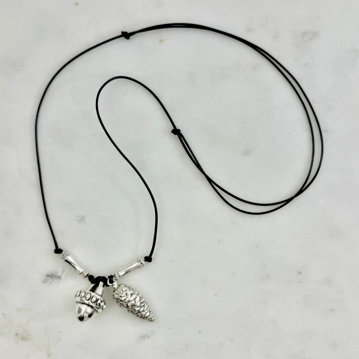 silver pendant necklace: με black cord με δύο silver-tone charms: ένα βελανίδι και ένα κουκουνάρι, σύμβολα της φύσης και του φθινοπώρου